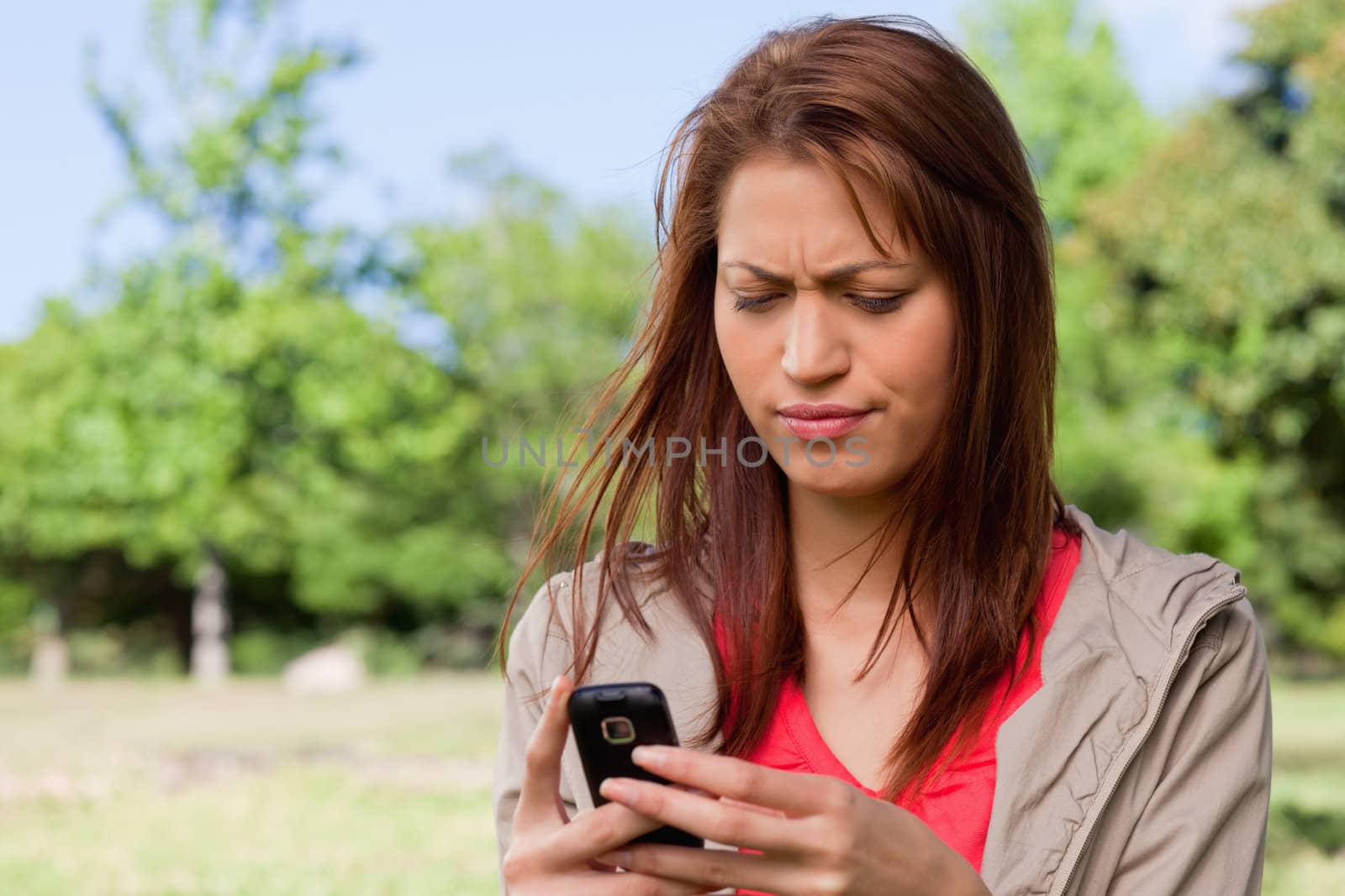 Woman with a cautious expression reading a text message in a bright parkland area 