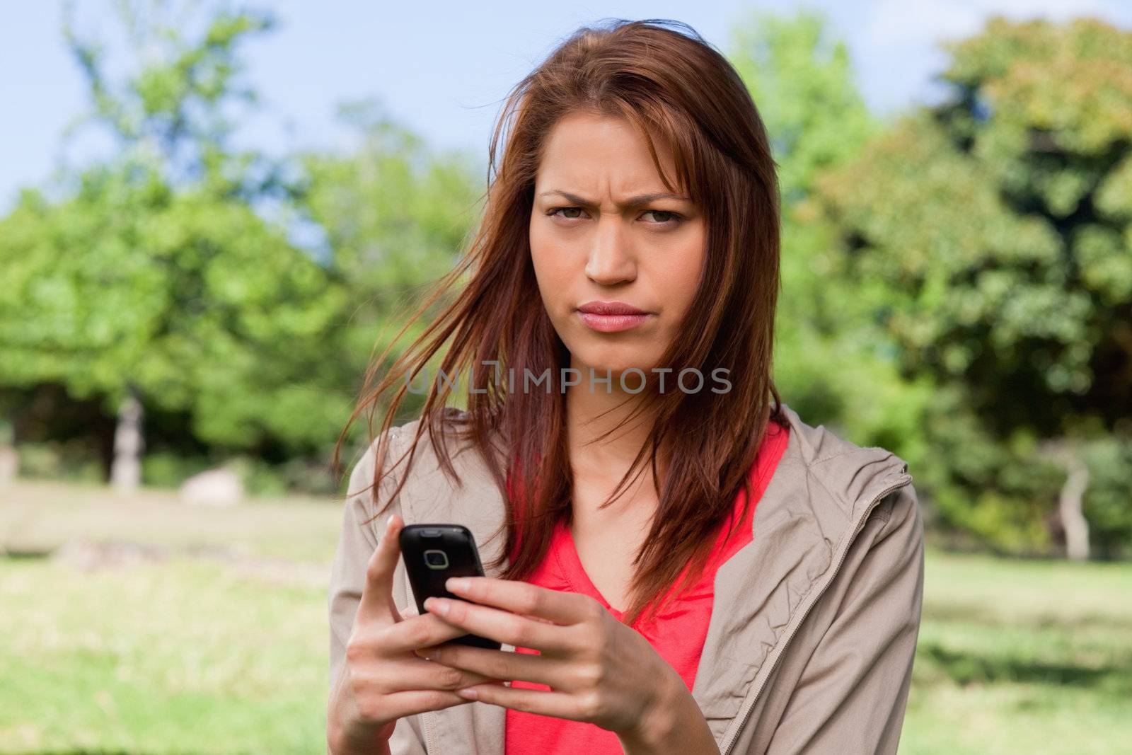 Young woman with a serious expression holding a phone in a sunny park