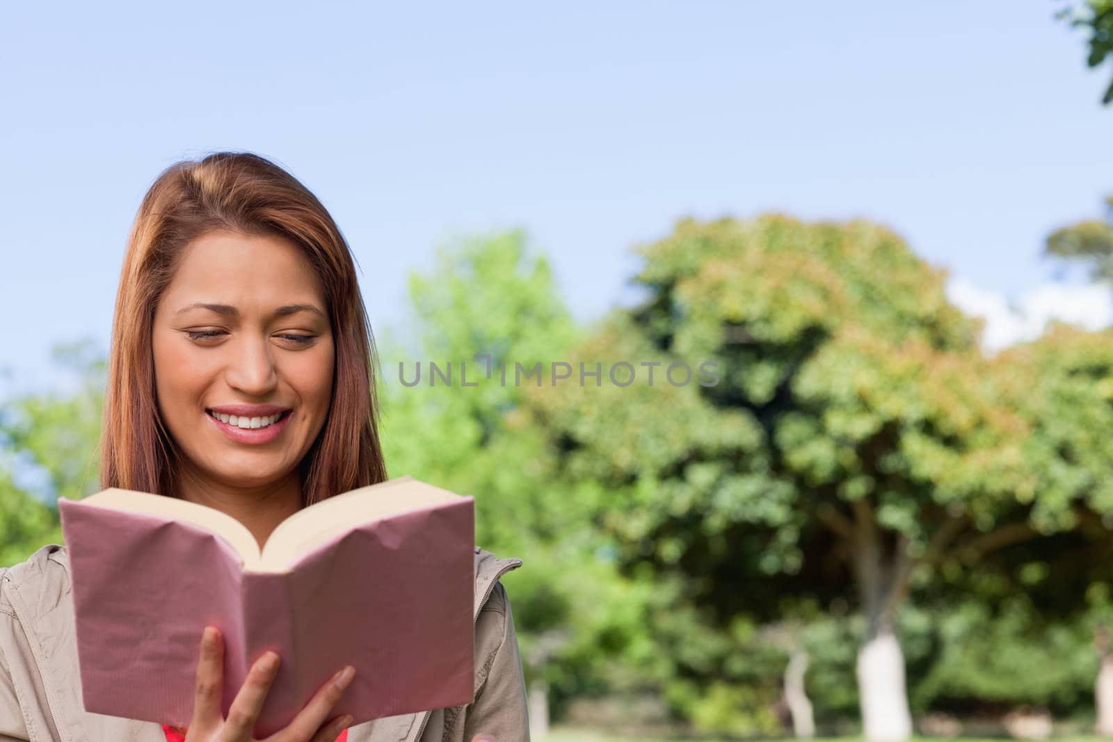 Young woman blissfully reading the book in her hands while in a sunny area surrounded by trees