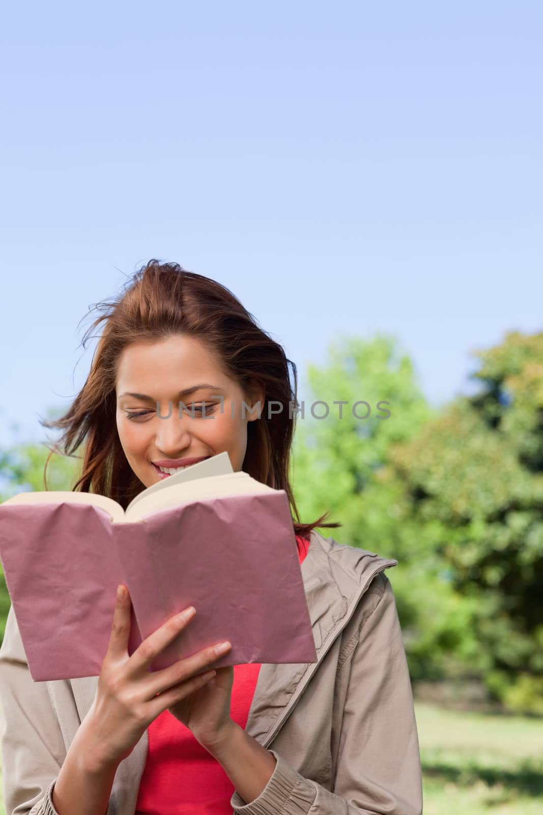 Young woman joyfully reading a book with the wind blowing through her hair in a bright parkland area