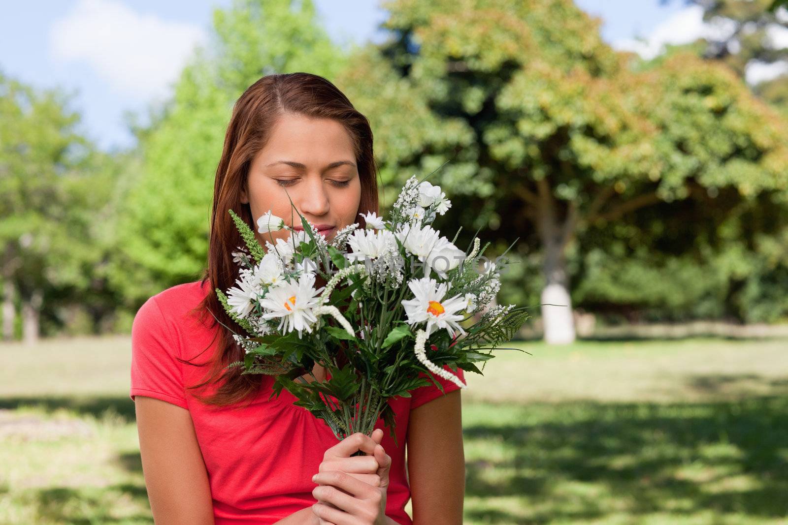 Woman smelling a bunch of flowers while standing in a park by Wavebreakmedia