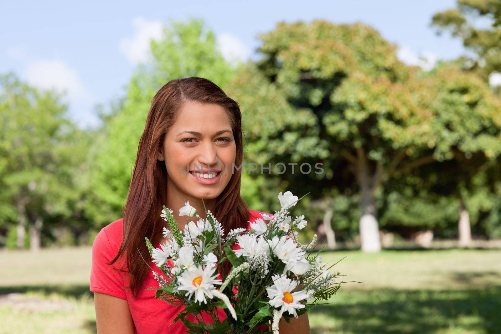 Woman looking into the distance and holding a bunch of flowers by Wavebreakmedia