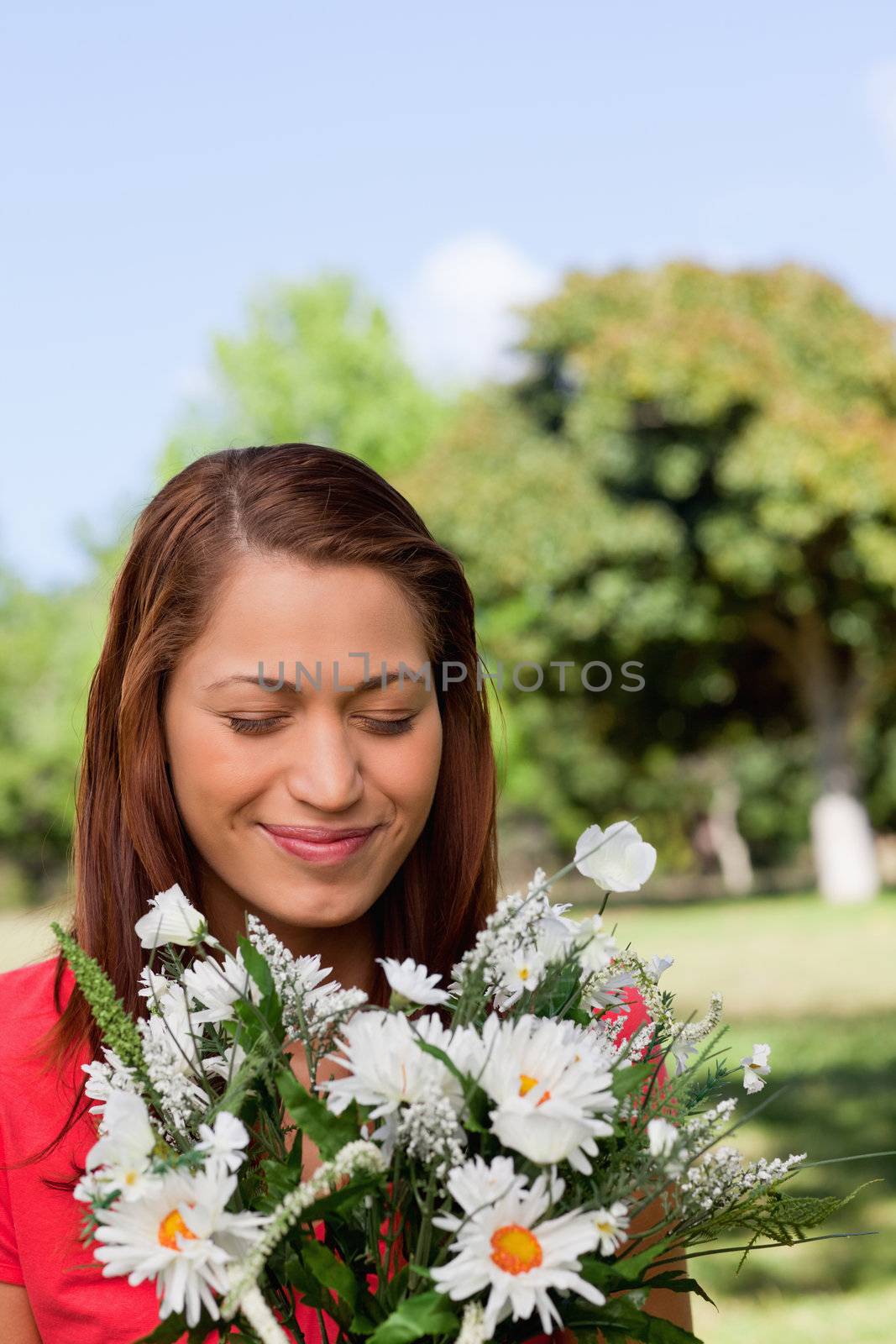 Young woman looking at a bunch of flowers while standing in a sunny parkland area