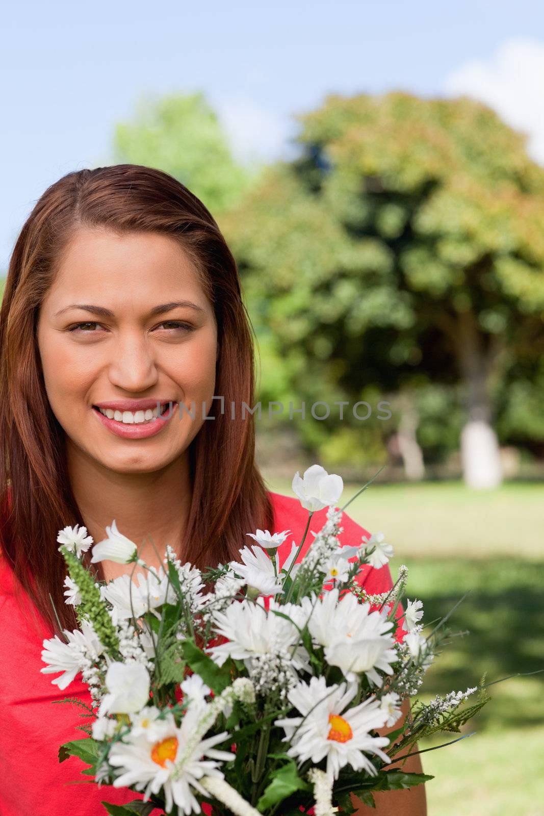 Young woman with the sun shining on her face, looking ahead while holding a bunch of flowers