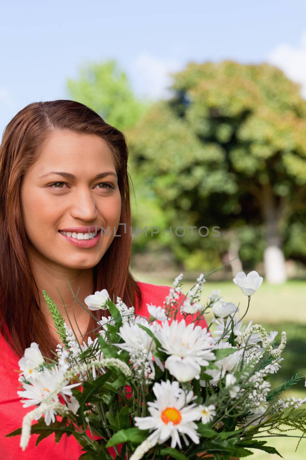 Woman looking towards the side while holding a bunch of flowers and and standing in an open area surrounded by trees