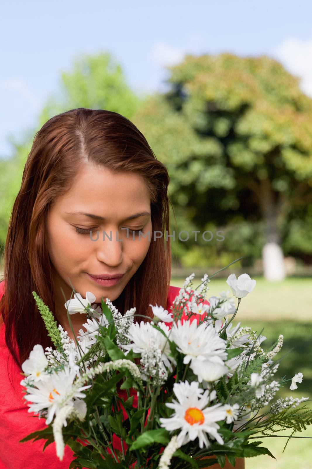 Young woman happily looking down towards a bunch of flowers while standing in an open grassland area