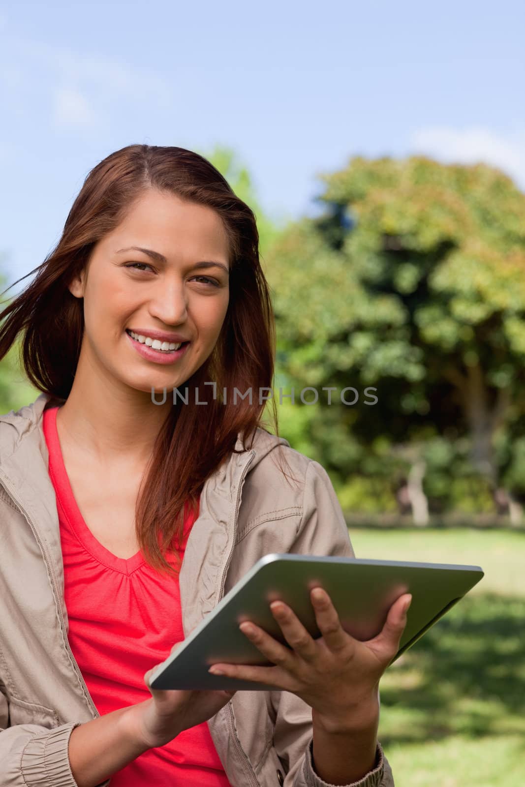 Young woman smiling and looking into the distance while she uses a tablet in a sunny park