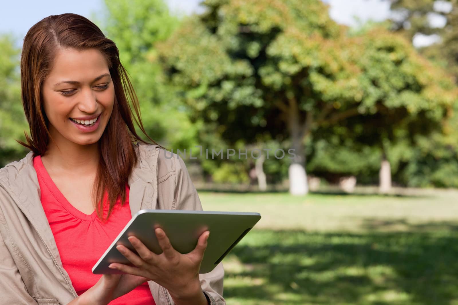 Young woman smiling enthusiastically while using a tablet in a sunny grassland area