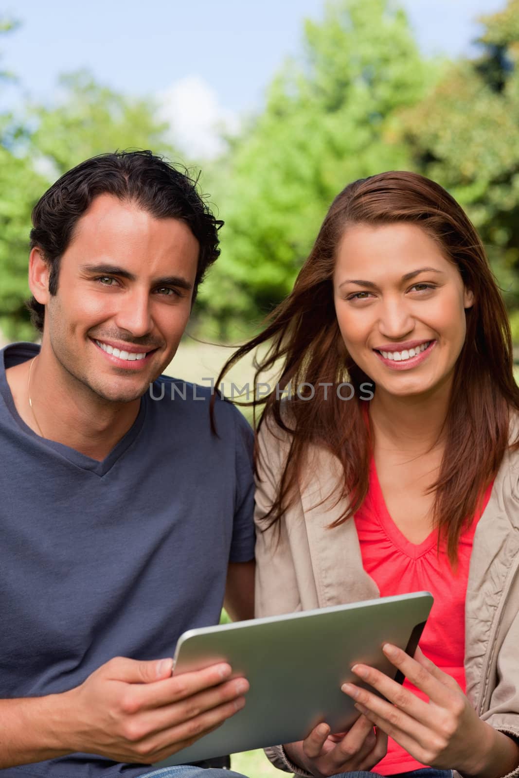 Man and a woman look ahead while holding a tablet in a sunny parkland environment