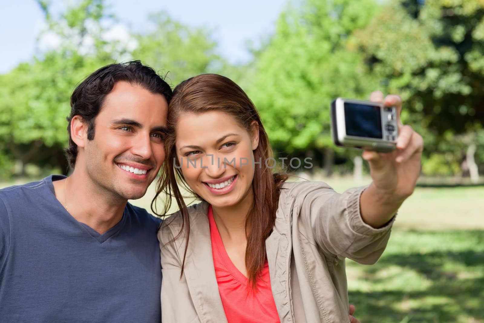Woman holds a camera at arms reach to take a picture of her friend and herself in an open grassland environment