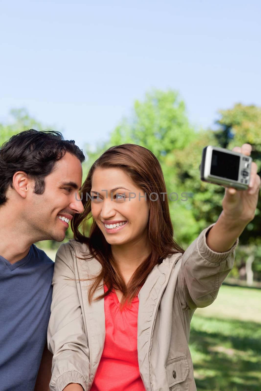 Young woman and her friend look at each other while she takes a photo of them together using her camera