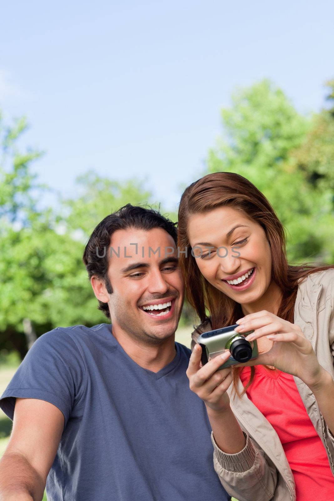 Two friends smiling happily as the look at the photo collection in a camera while sitting in a sunny park
