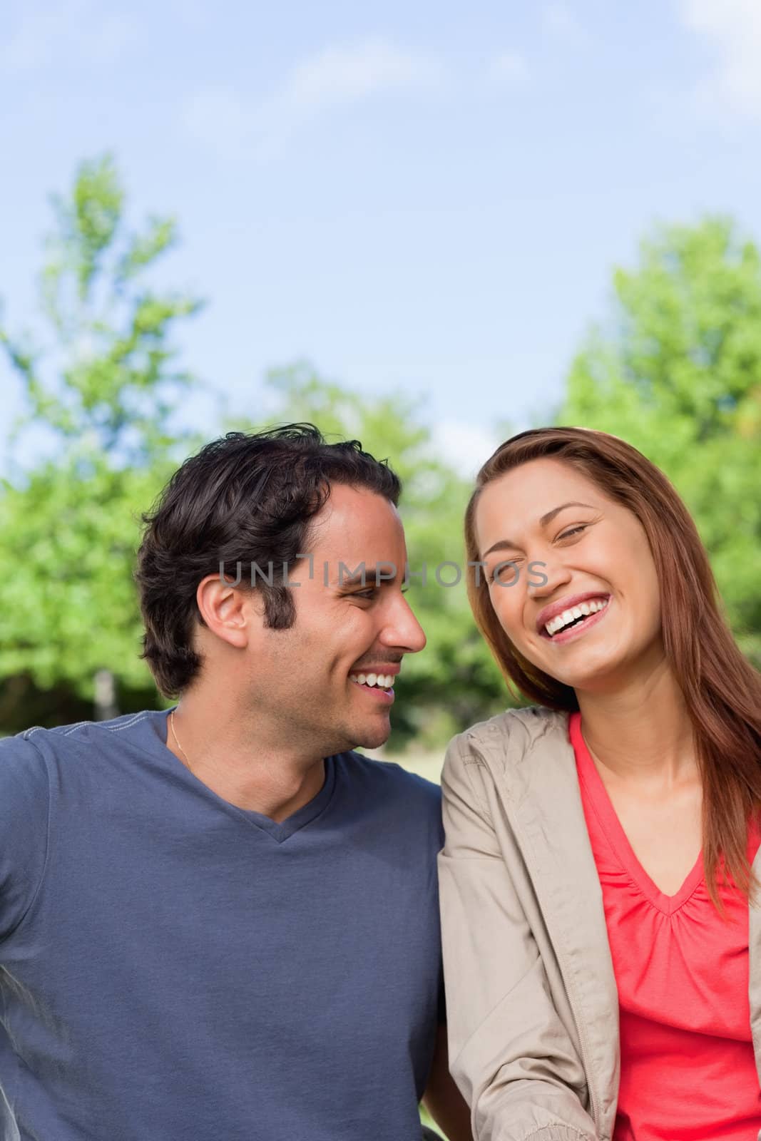 Man happily looking his friend as she is laughing joyfully in a park on a sunny day