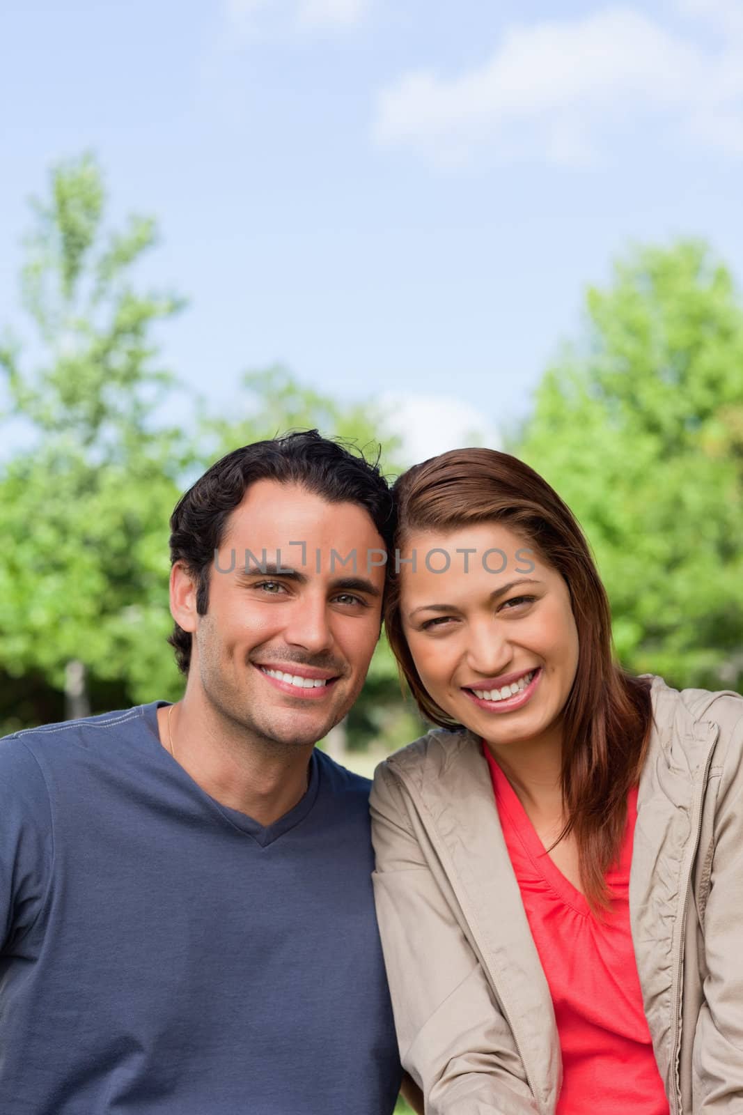 Two friends smiling as the look ahead while sitting side by side in a bright park environment