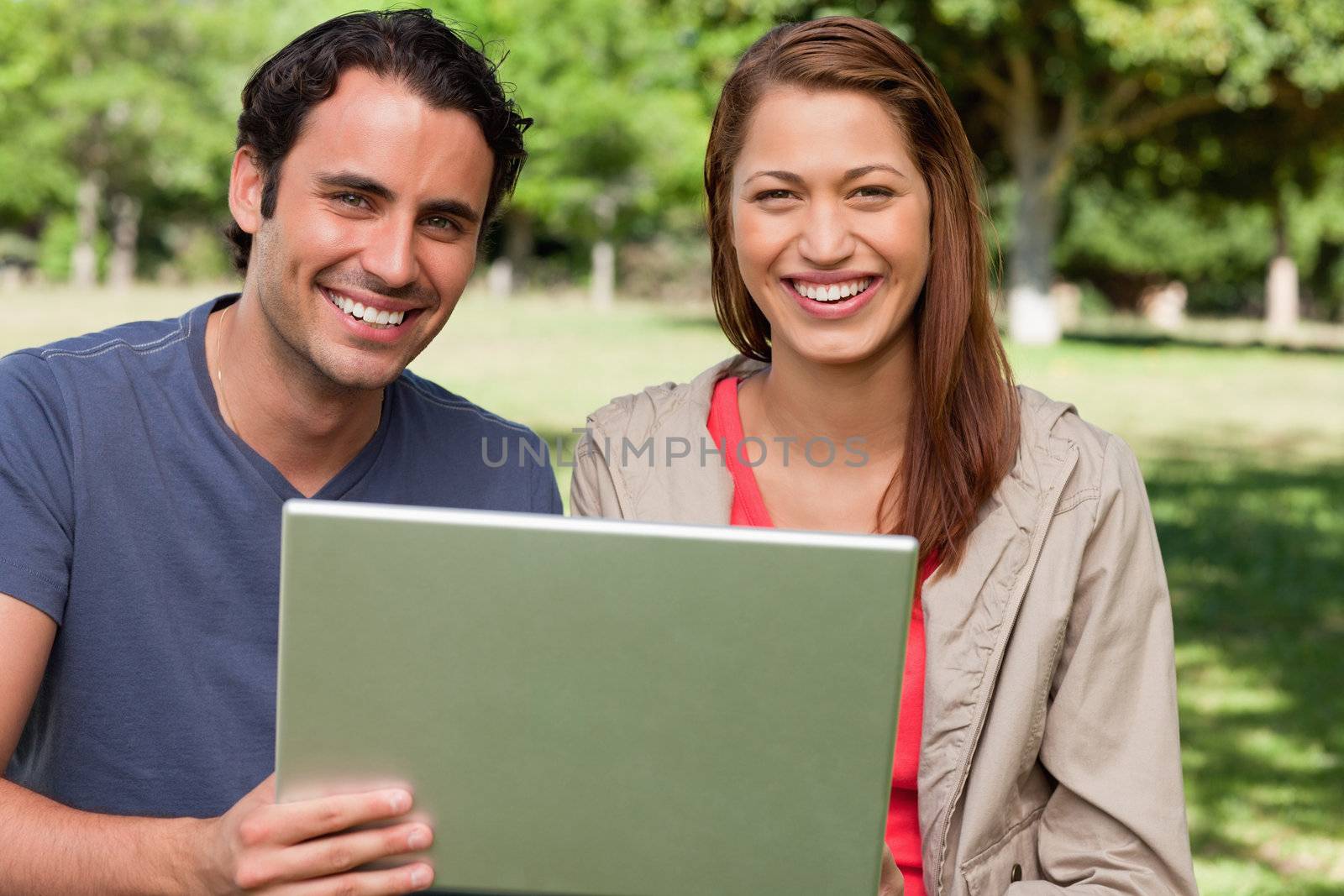 Two smiling friends looking ahead as they hold a tablet by Wavebreakmedia