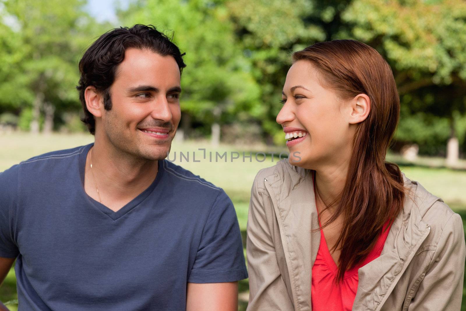 Man is grinning while he watches his friend who is gleefully laughing in a bright grassland area