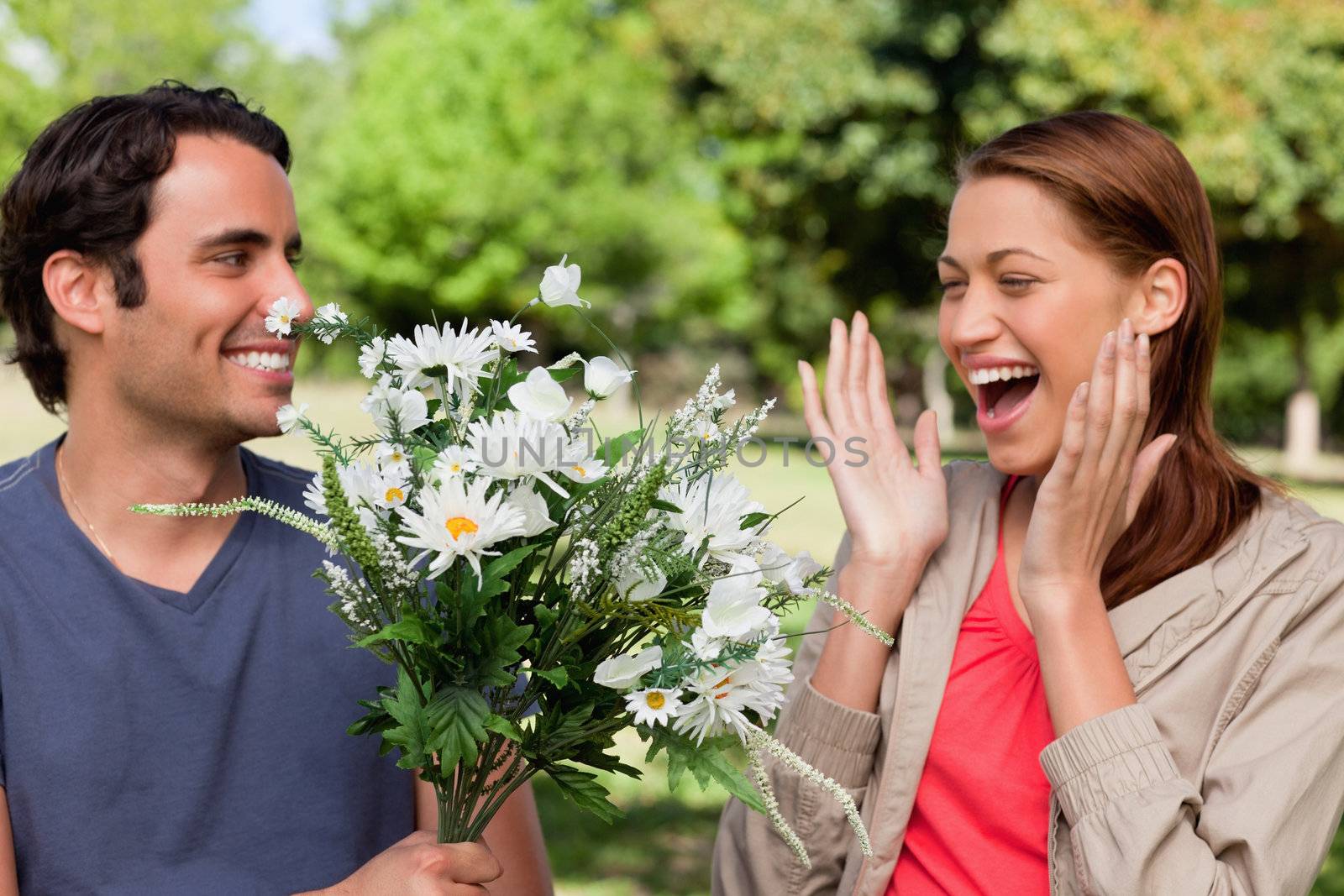 Woman laughing excitedly as she is presented with a bunch of flowers by her friend in a sunny parkland