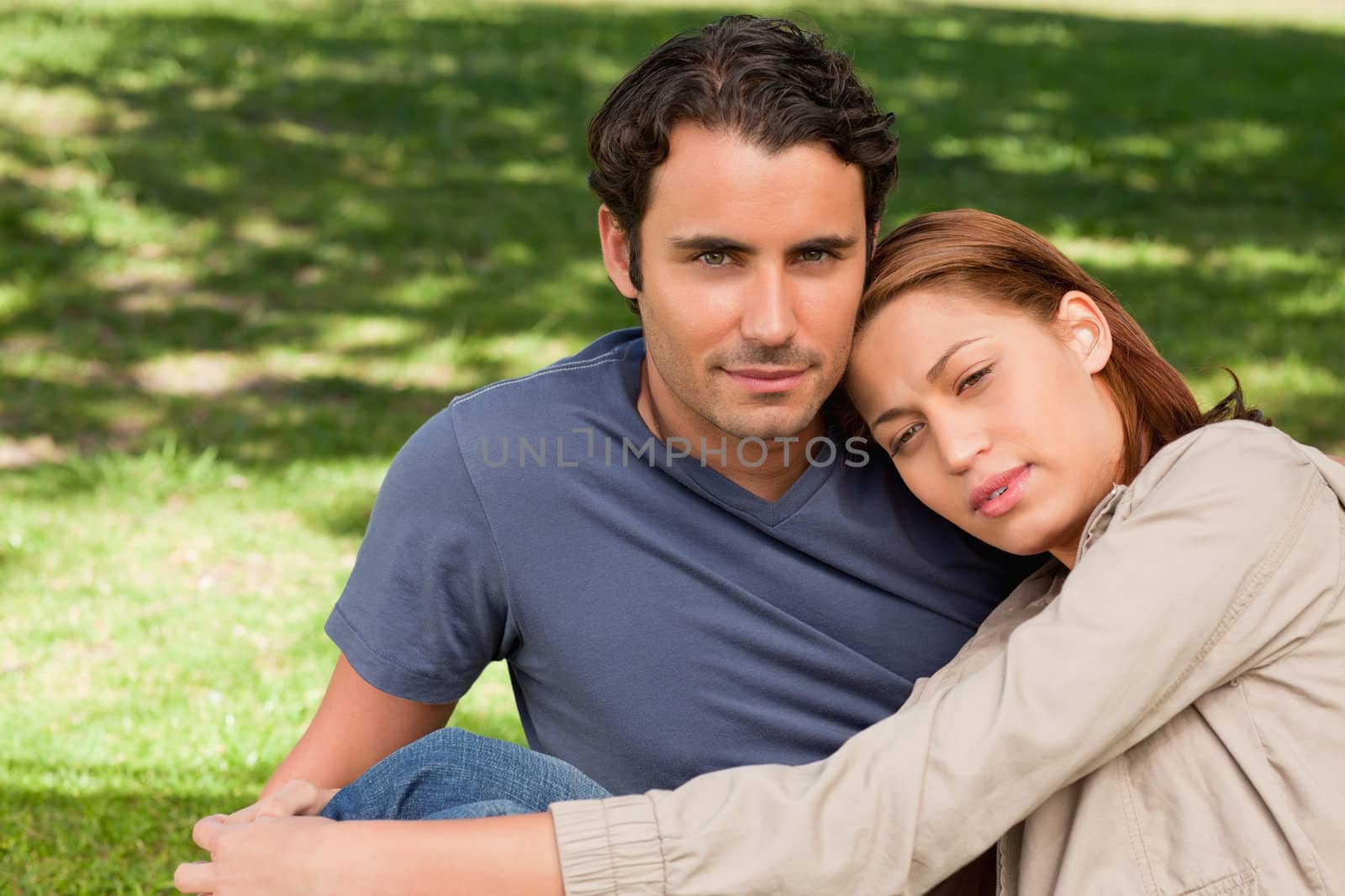 Man looking towards the sky with his friend who is resting her head on his shoulder as the sit on the grass