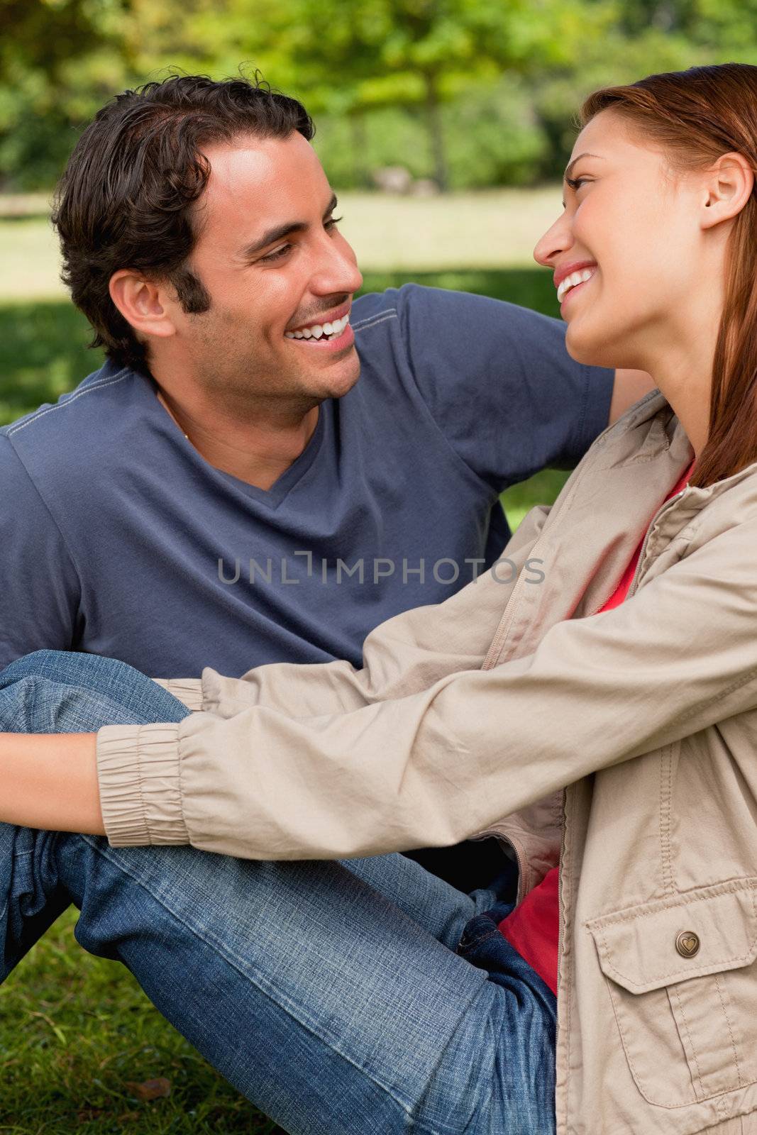 Two friends with delighted expressions look into each others eyes while they are both sitting on the grass