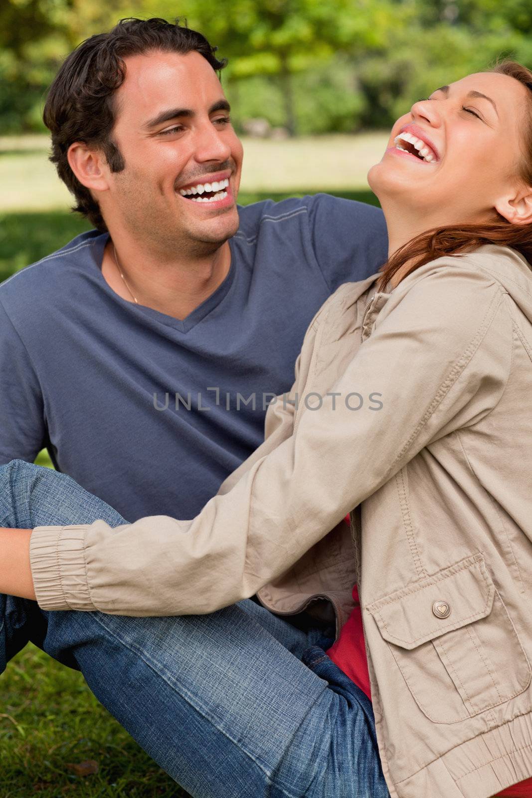Two friends enthusiastically laughing as they are sitting next to each other on the ground in a bright grassland