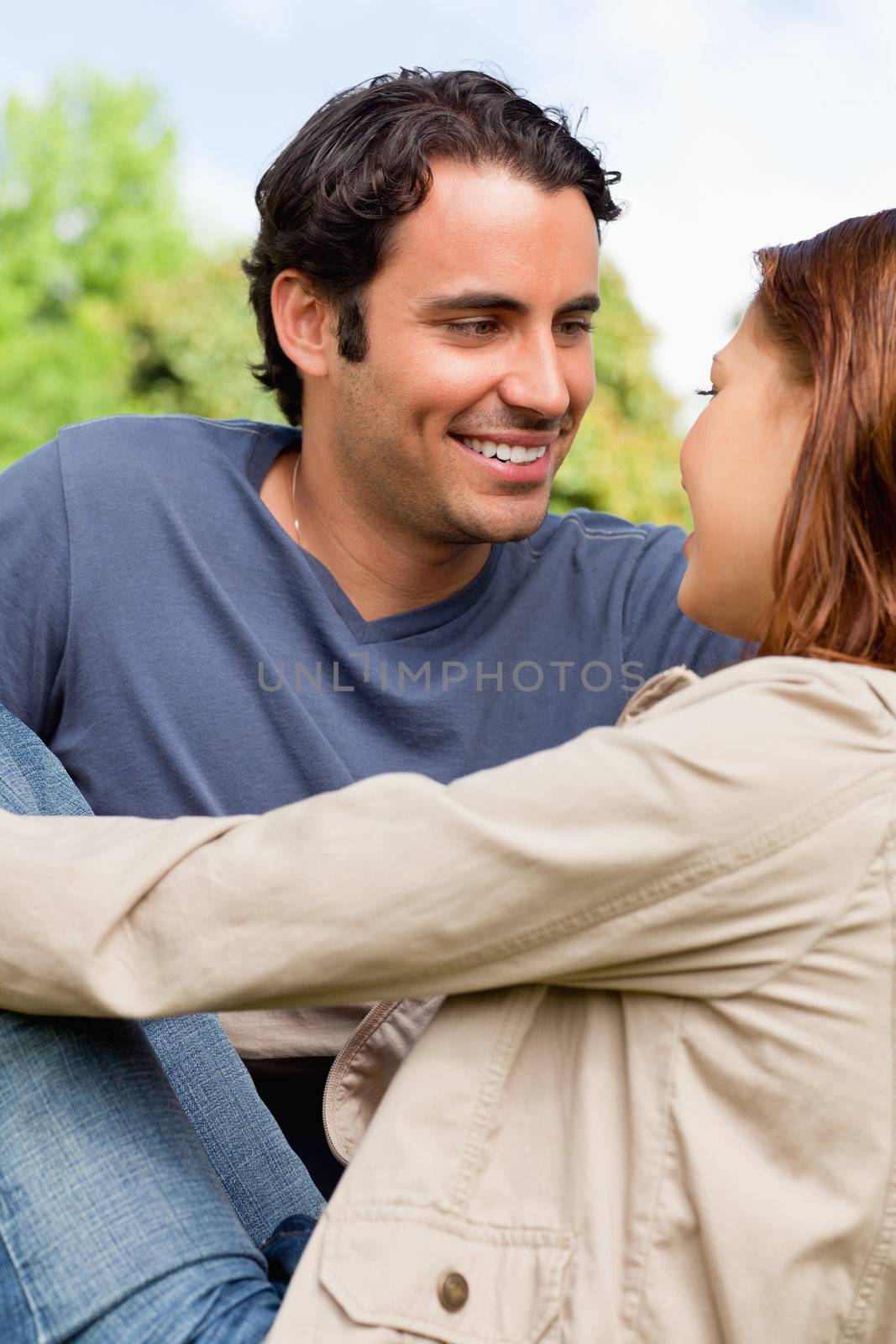 Two friends happily looking into each others eyes as they sit next to each other on the ground in a grassland