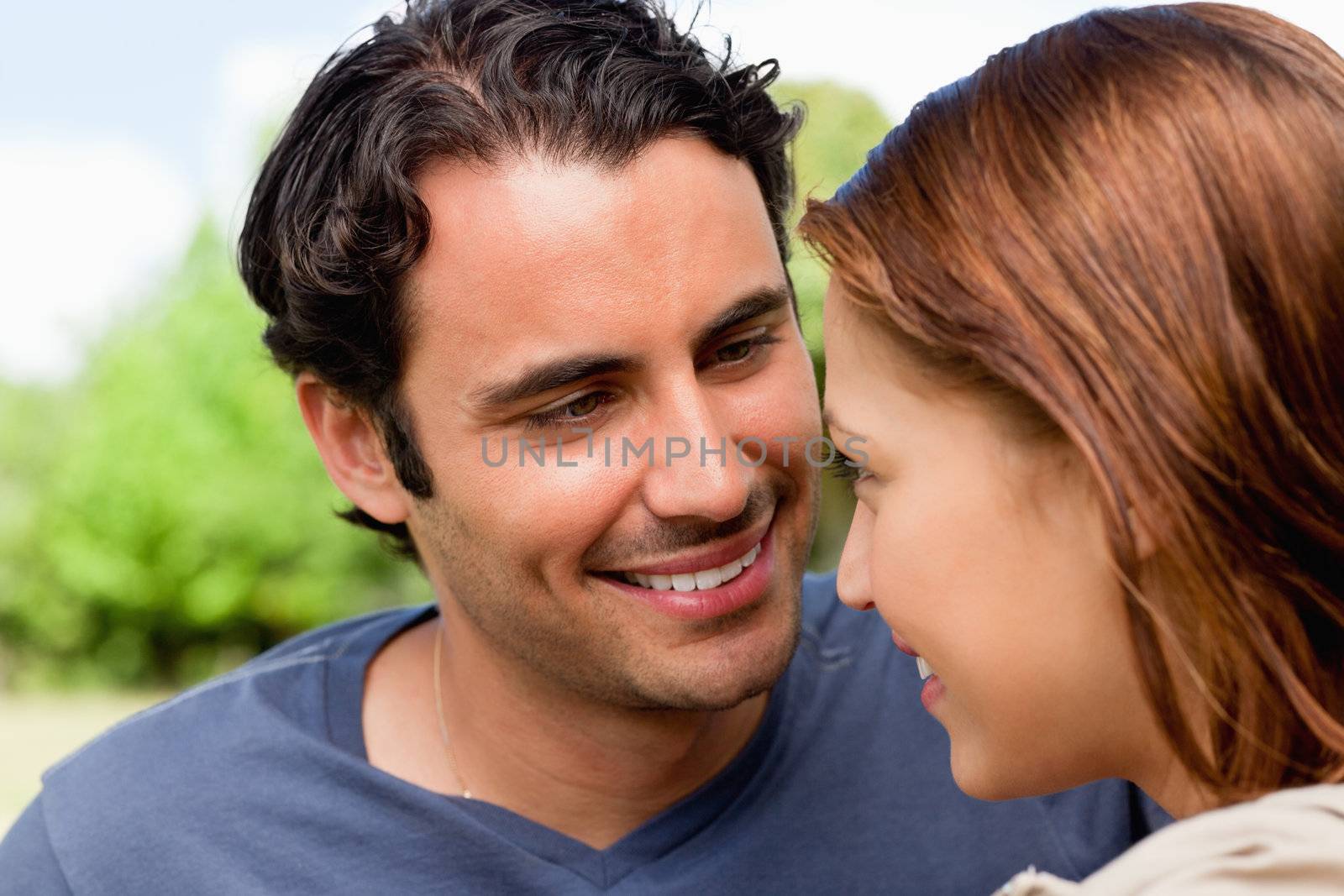Two friends smiling as they look into each others eyes while they are both sitting on the grass in a park
