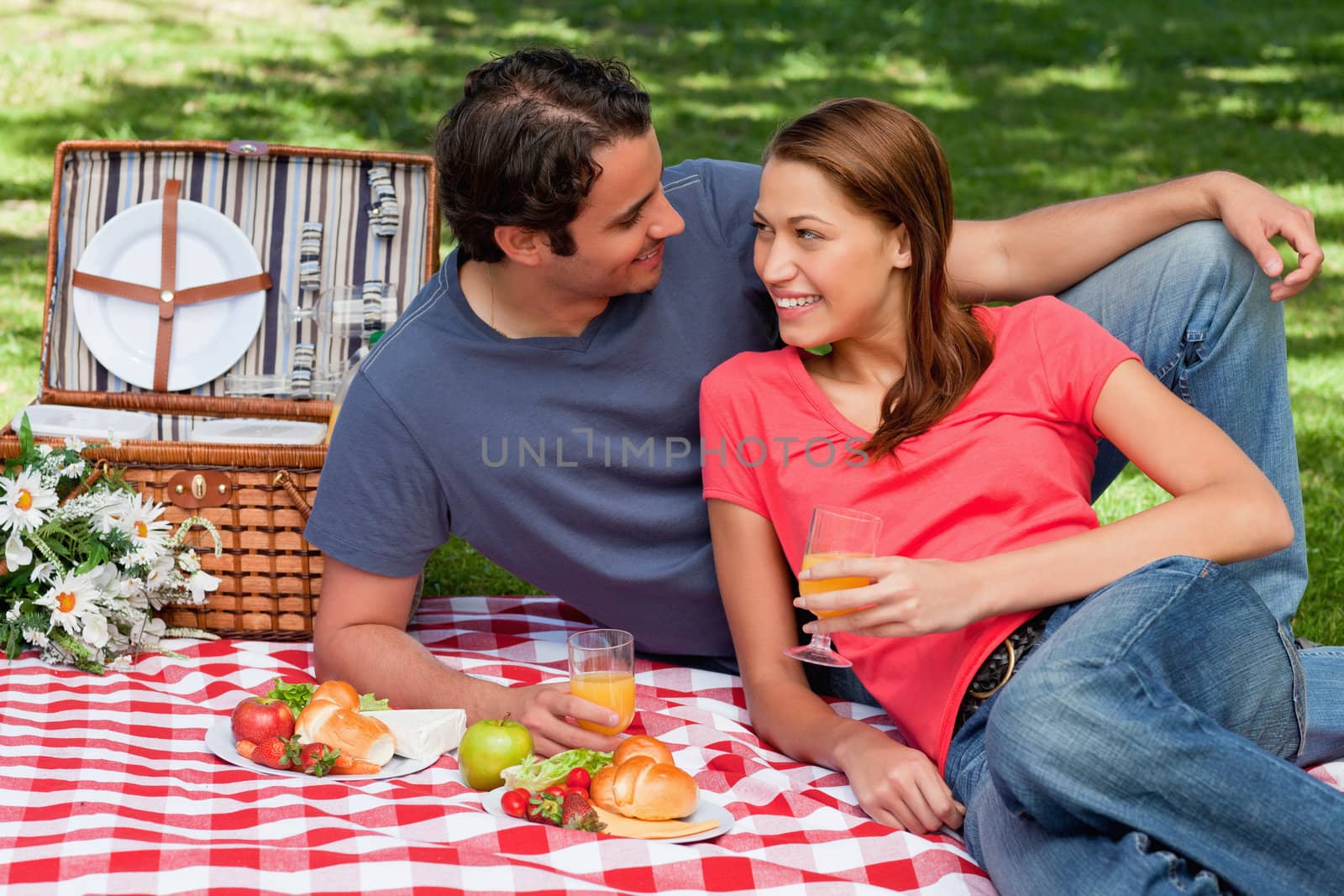 Two friends holding glasses while looking into each others eyes and lying on a blanket with a picnic basket