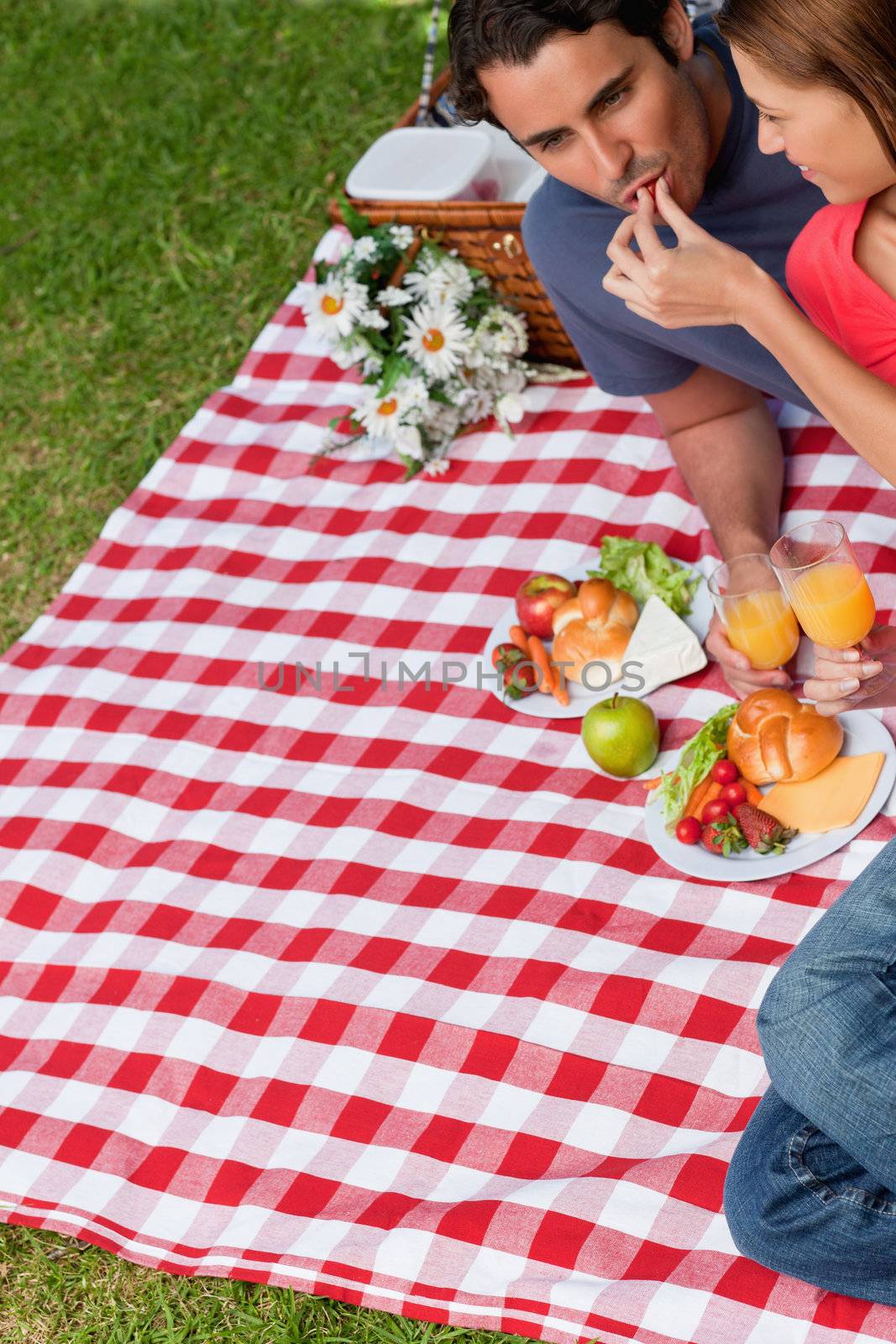 Young woman feeding her friend as they lie next to each other on a blanket with a picnic basket and food