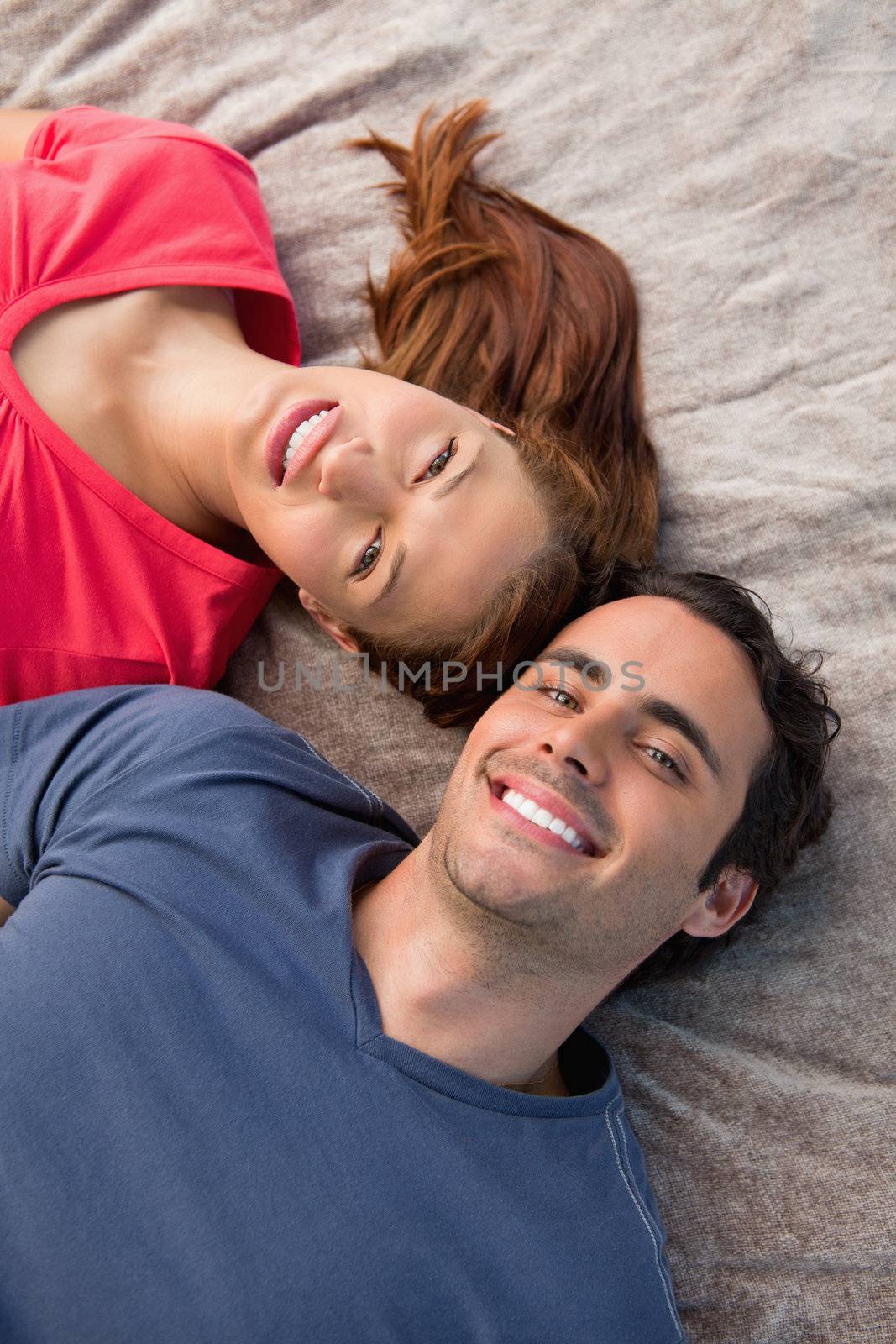 Close-up of two smiling friends lying next to each other as they look into the sky while on a grey quilt