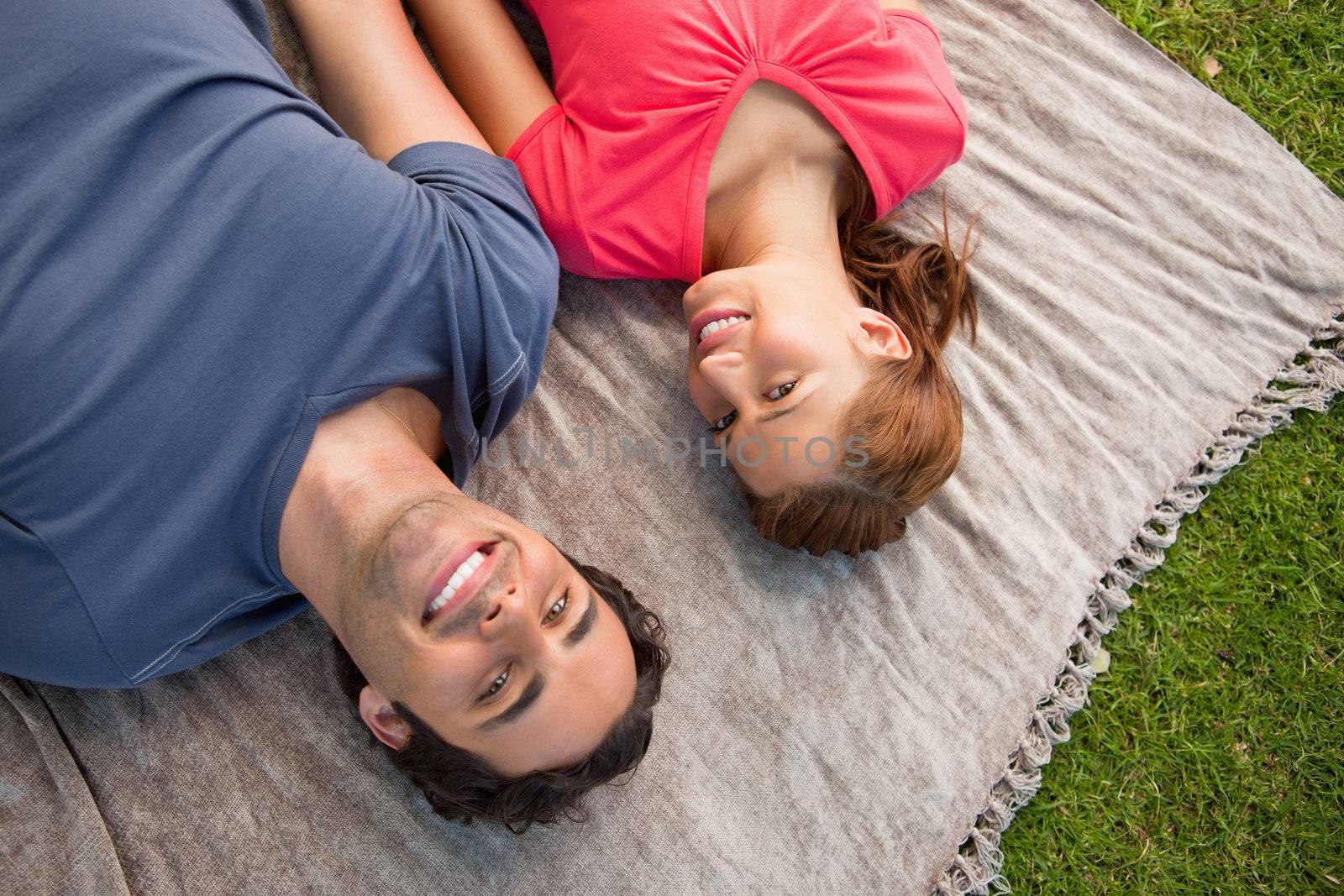 Two smiling friends looking towards the sky while lying side by side on a quilt