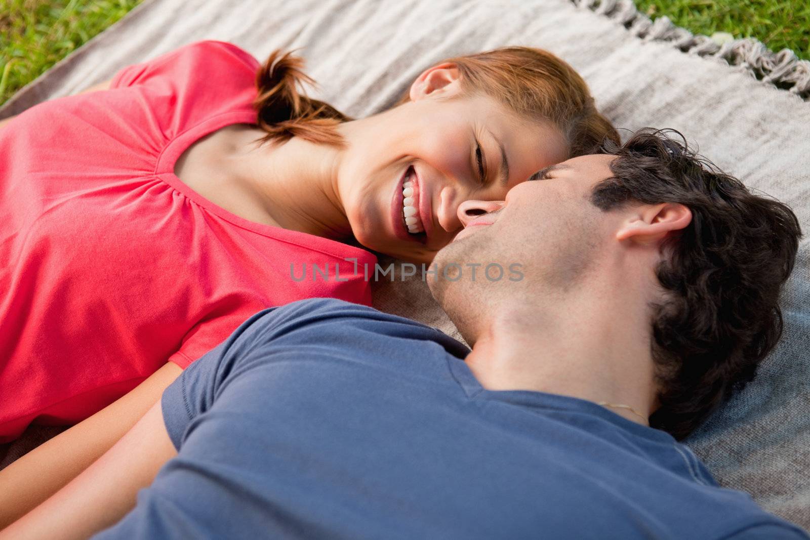 Woman smiling with her eyes closed while lying with her friend on a grey quilt