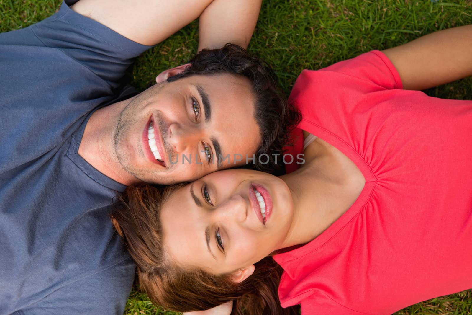 Two friends smiling while looking towards they sky as they lie head to shoulder with an arm behind their head on the grass