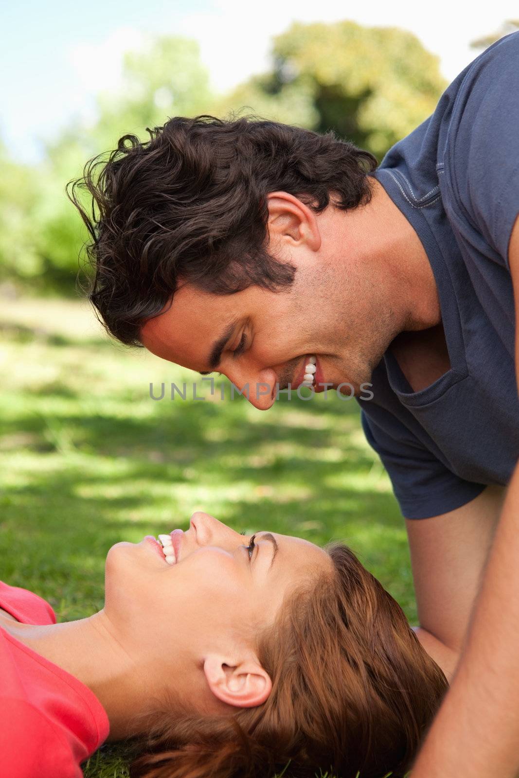 Man smiling as he looks down towards his smiling friend who is lying on the grass