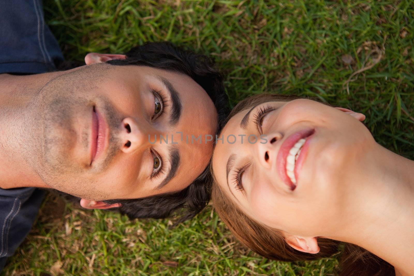 Close-up of two friends smiling while looking at each other as they lie head to head on the grass