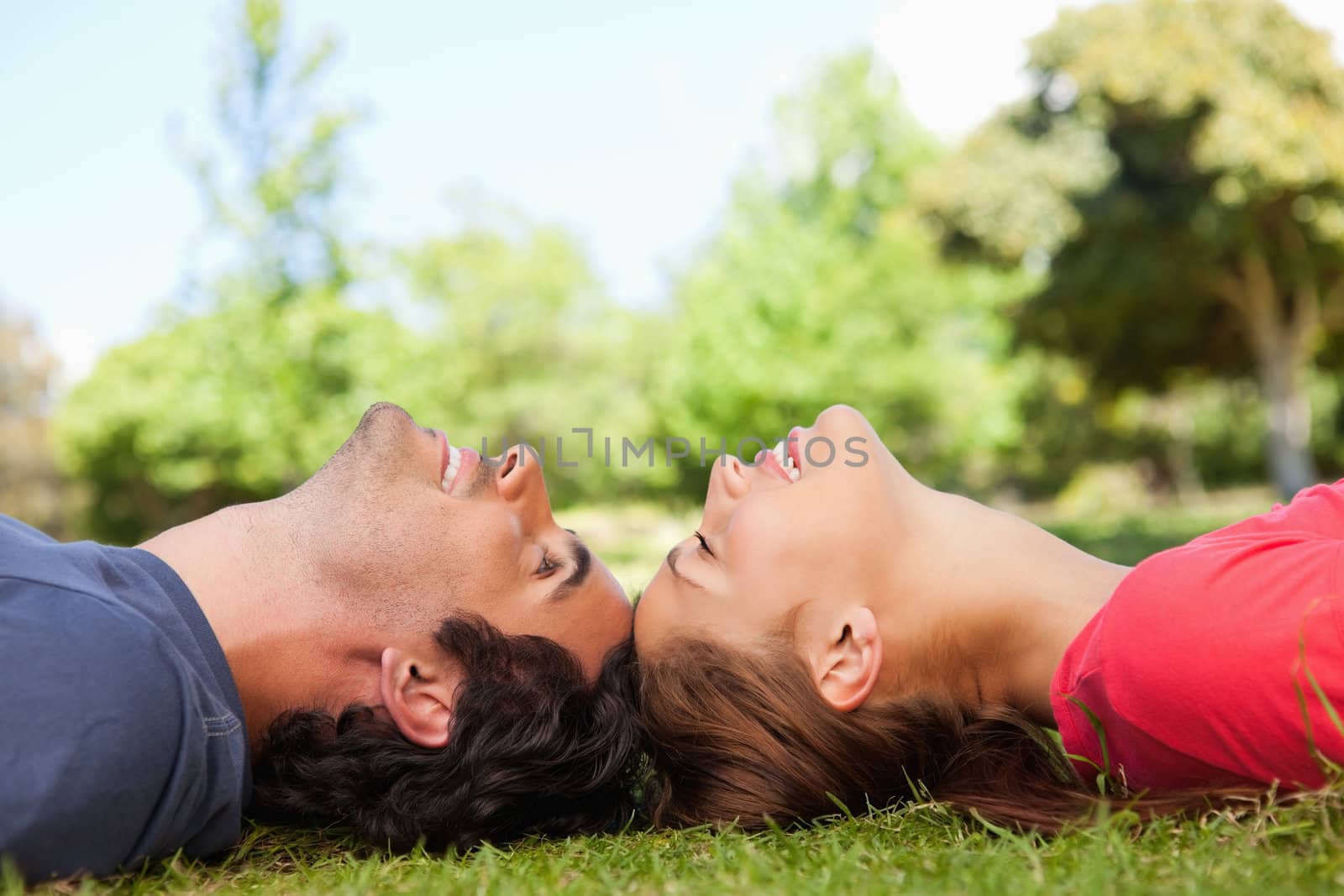 Two friends smiling with their eyes closed as they lie head to head on the grass