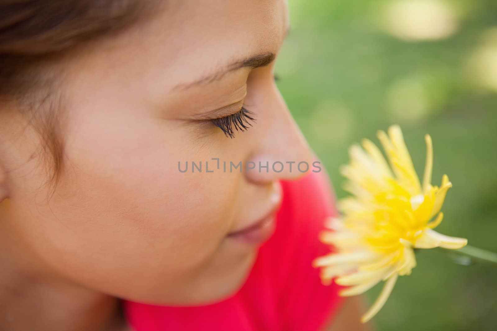 Woman closing her eyes while smelling a yellow flower with grass in the background