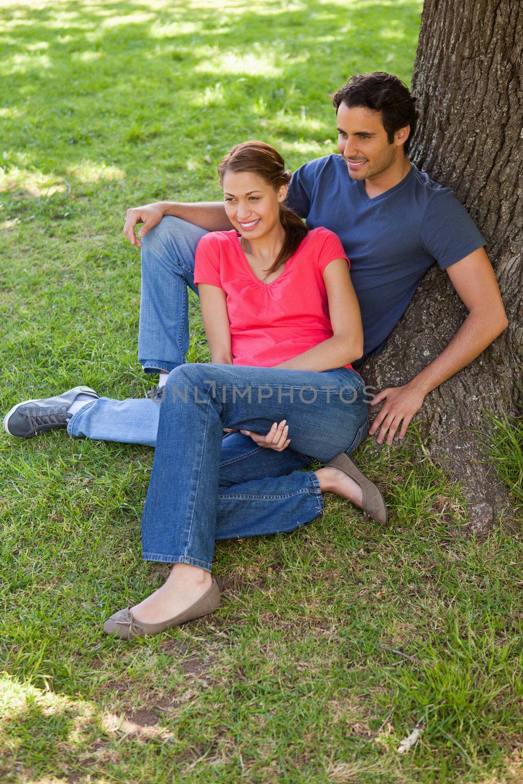 Two friends smiling as they sit together against the trunk of a tree