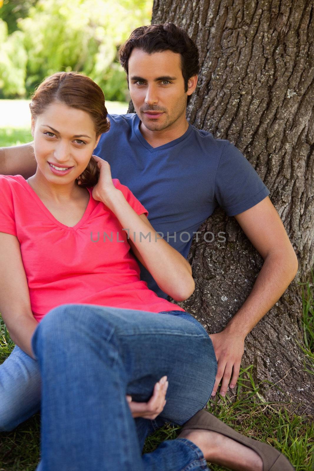 Two friends looking in front of them while sitting together against the trunk of a a tree