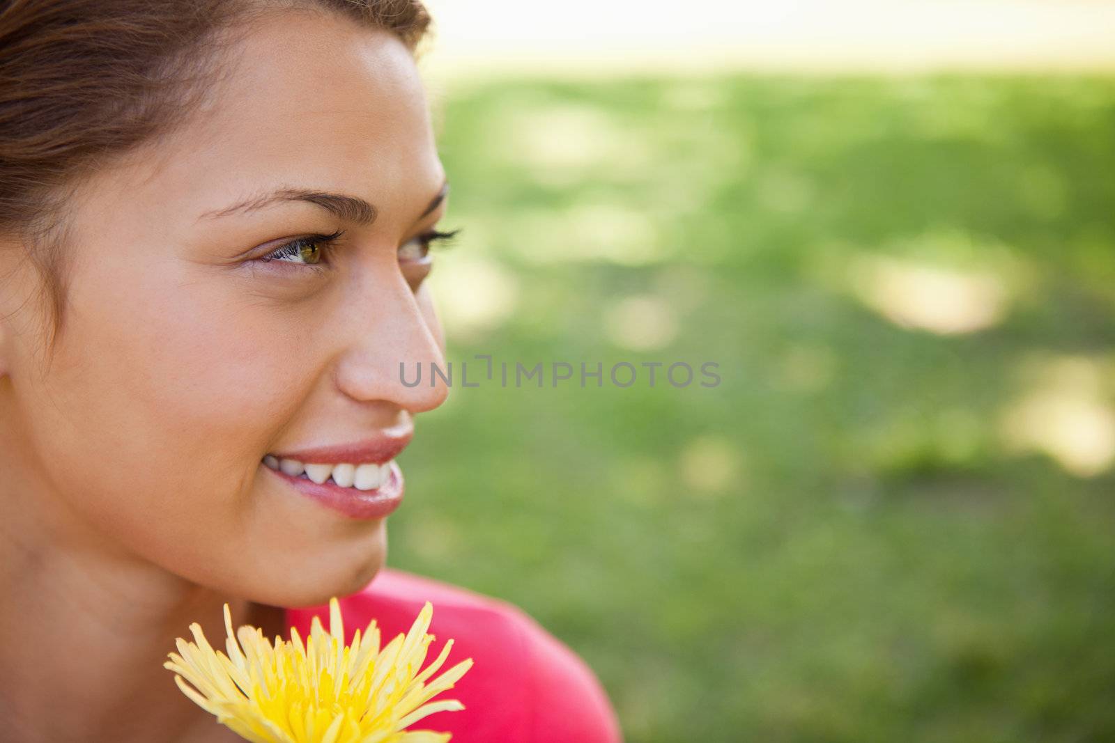 Smiling woman looking towards the side while holding a yellow flower with grass in the background