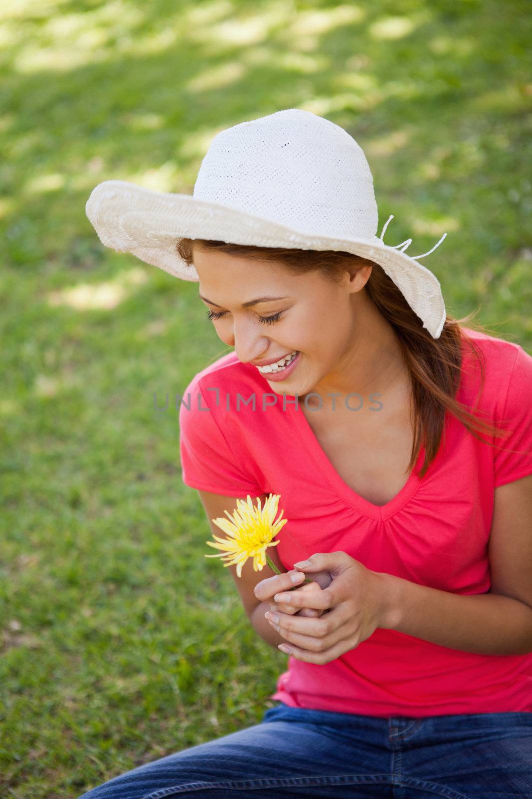 Woman laughing while wearing a white hat and holding a yellow flower as she sits on the grass