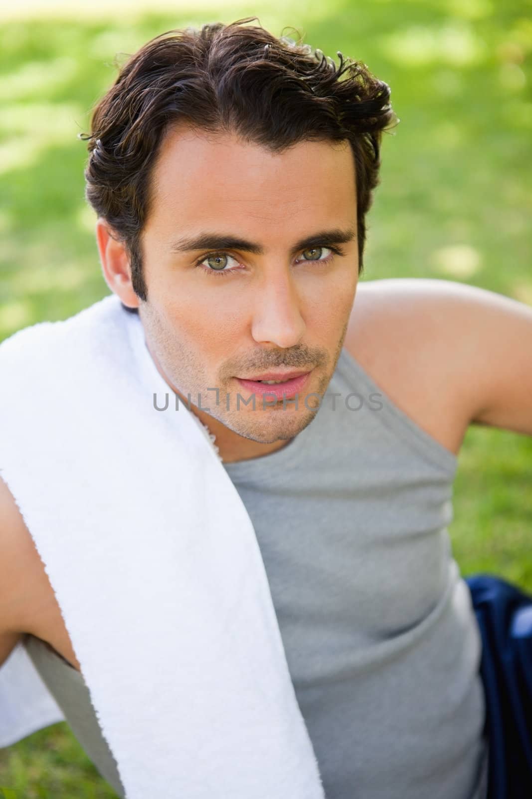 Man looking at the camera with a towel resting on his shoulder as he sits on the grass