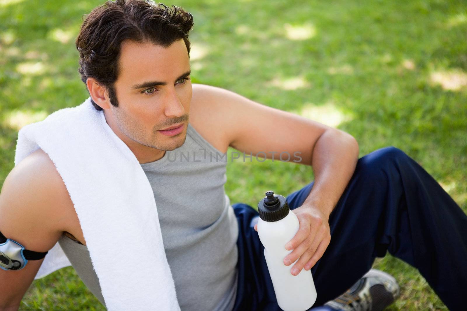 Man with a white towel on his shoulder looking straight ahead while holding a sports bottle