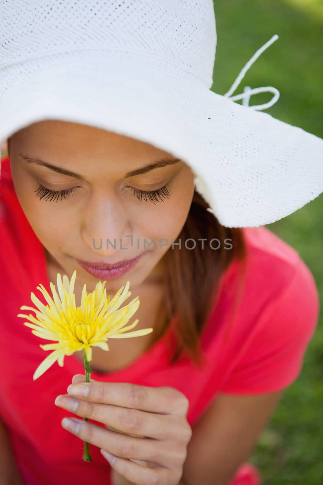 Woman wearing a white hat while smelling a yellow flower while looking down at the flower, 