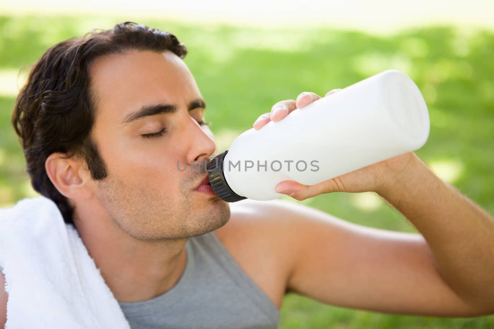 Man with a white towel on his shoulder drinking from a sports bottle while his eyes are closed