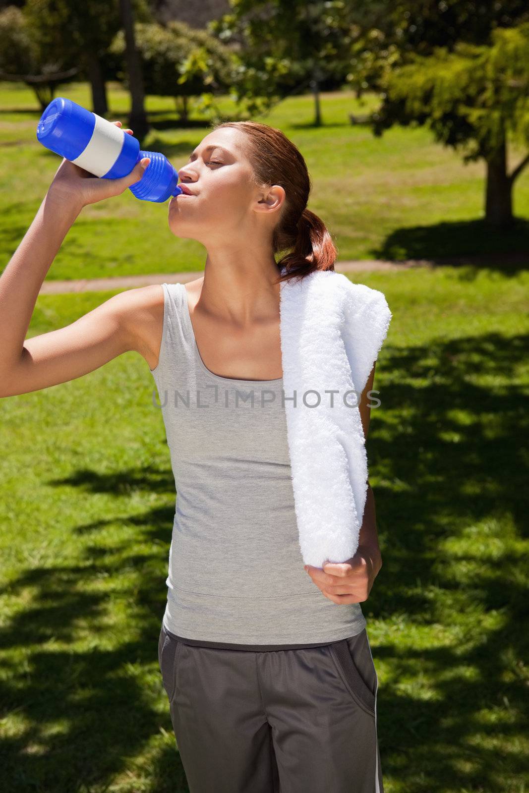 Woman with a white towel on her shoulder drinking from a blue sports bottle
