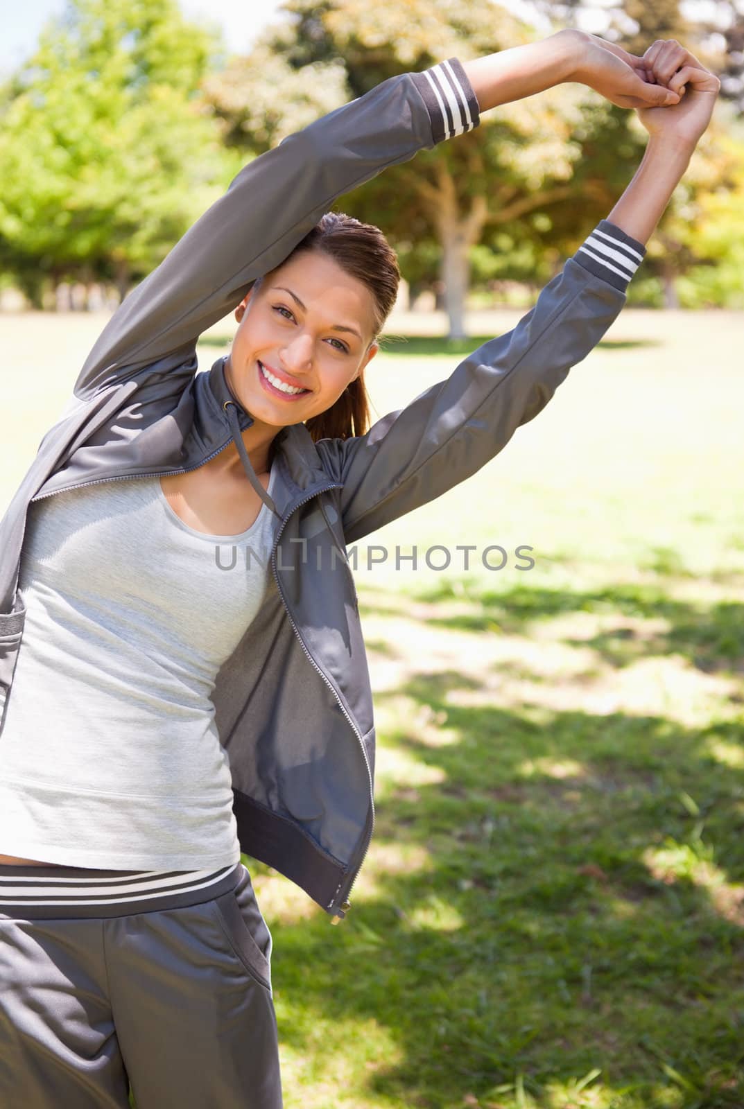 Woman smiling while  doing overhead stretches as she is standing in the grass