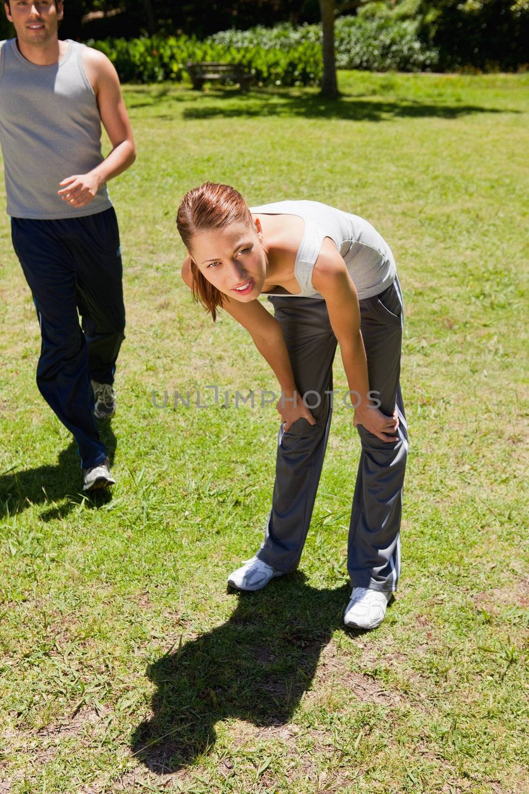 Woman bending over to recover while a man is jogging behind her on the grass