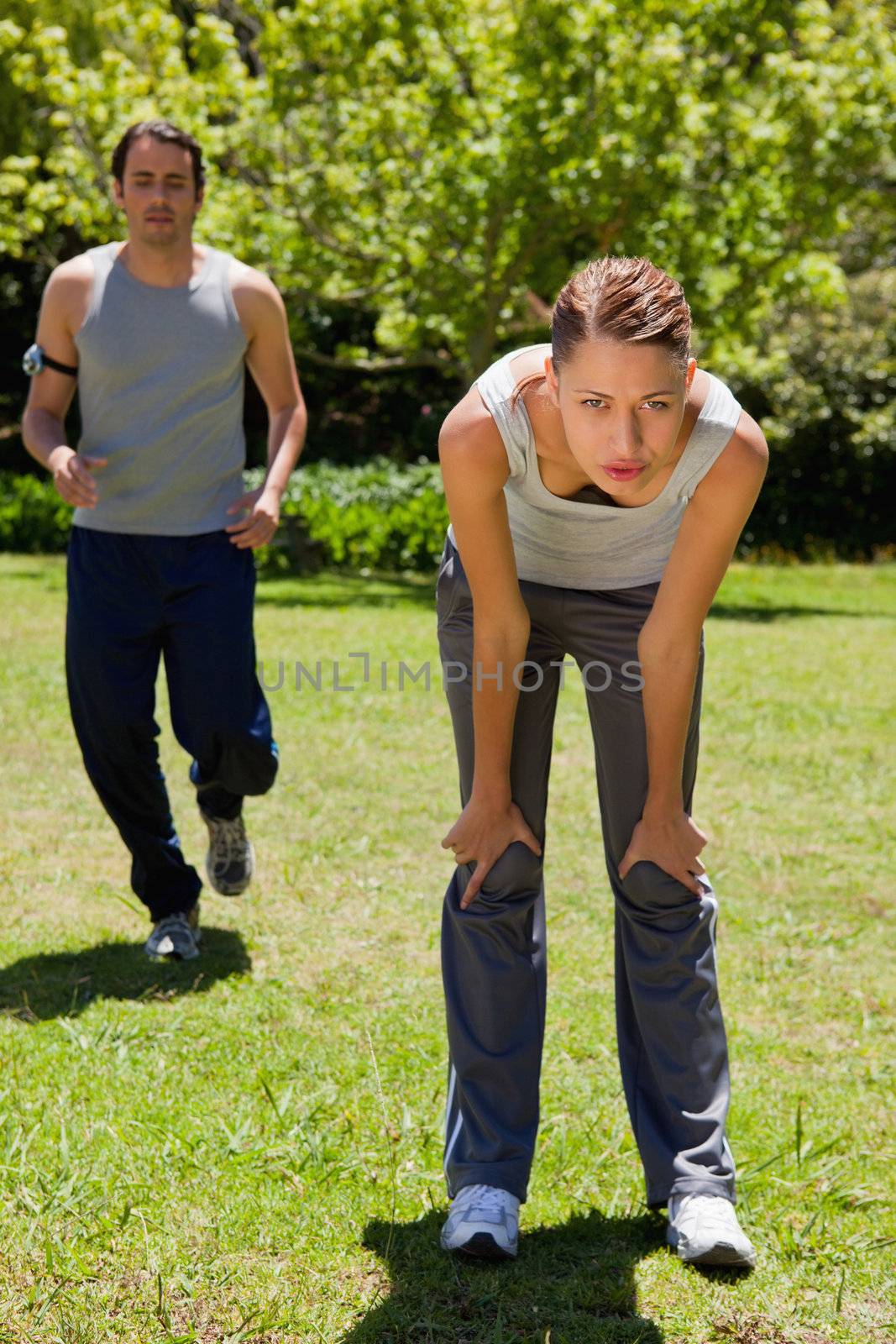 Woman bending over while a man is jogging in the background by Wavebreakmedia
