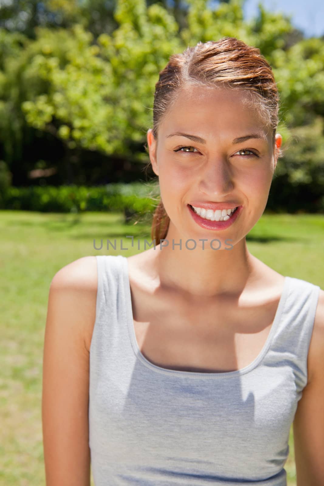 Woman dressed in workout gear smiling while looking straight ahead with trees and grass in the background