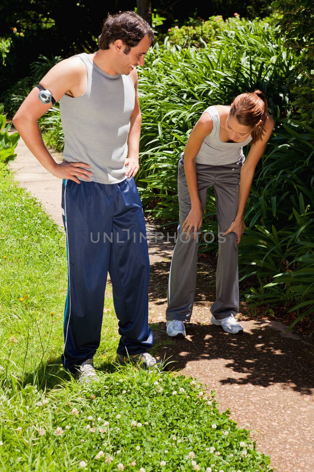 Man wearing a pedometer watching a woman as she is bent over while recovering next to bushes